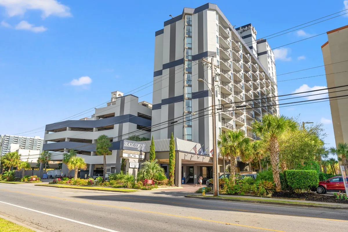 This exterior scene features the welcoming entrance of the resort, showcasing modern architecture, landscaped greenery, and clear entrance signage. The setting is vibrant and inviting, making it clear this is a hub for travelers and activity-seekers. The image radiates energy and accessibility, with hints of the beach atmosphere nearby.