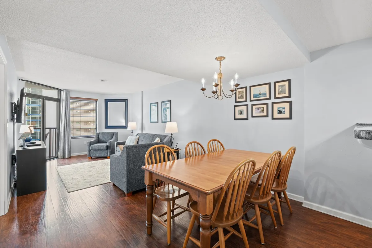 This image displays an inviting open-concept living and dining space. A stylish dining table sits beneath a chandelier, adjacent to a plush sofa and a television. The decor is comfortable and welcoming, perfect for family dinners or relaxing evenings.