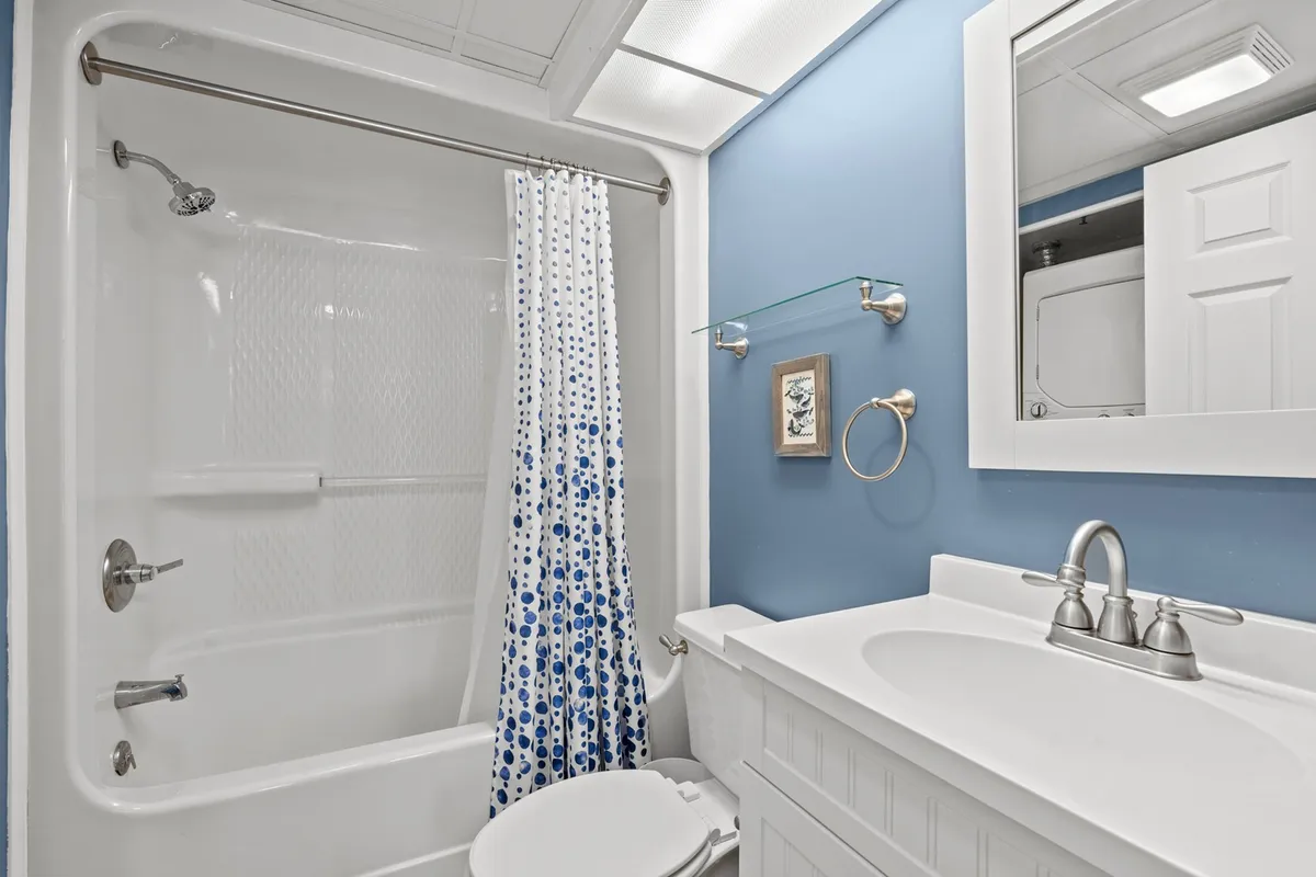 A modern bathroom with a crisp white vanity, blue accent wall, floral shower curtain, and a well-lit mirror. The design feels fresh and inviting, suggesting updated amenities and thoughtful touches.