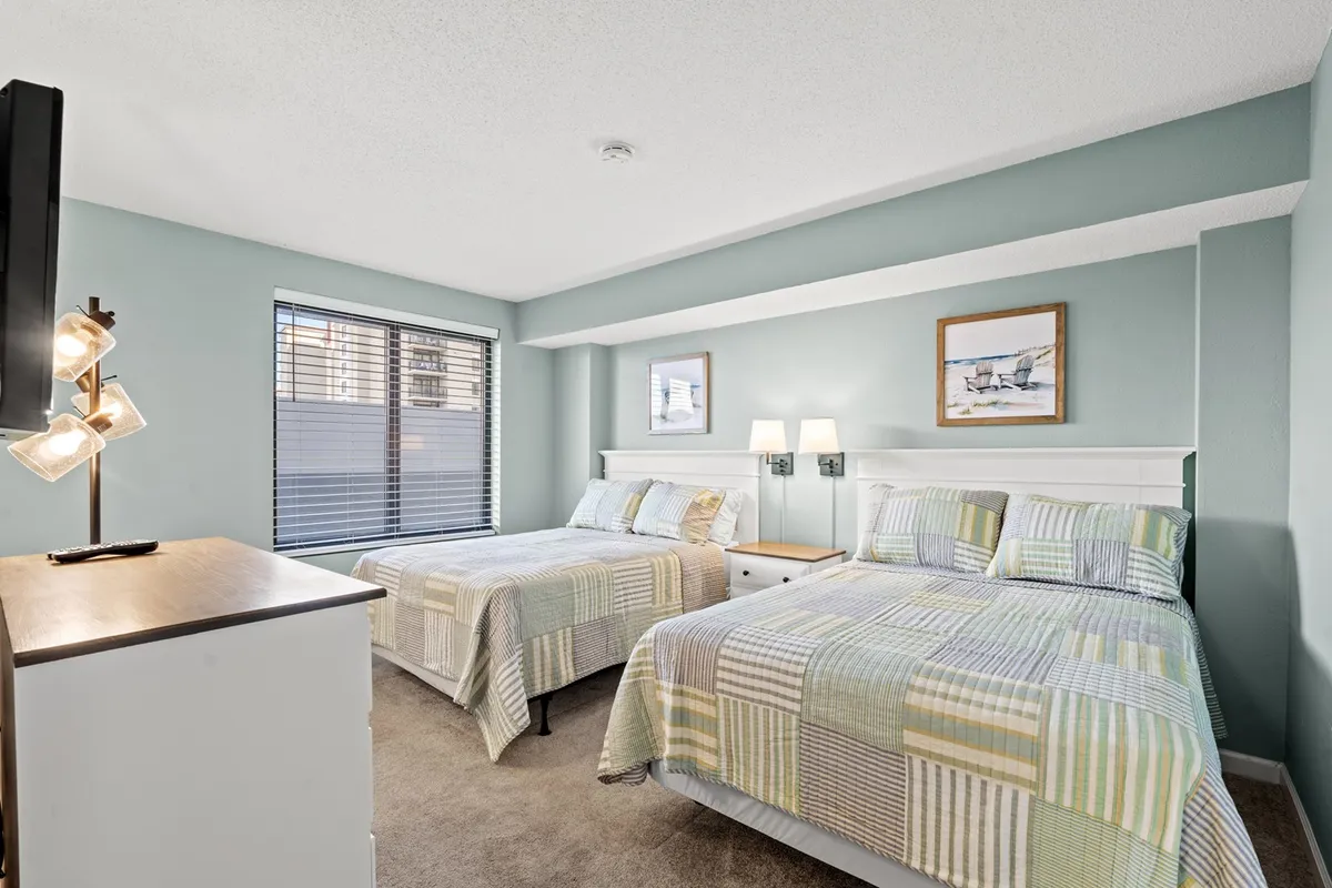 A spacious bedroom with two double beds, stylish decorative artwork above the beds, and a modern lamp. The room is well-lit and appears perfect for families or groups traveling together, offering both comfort and flexibility.