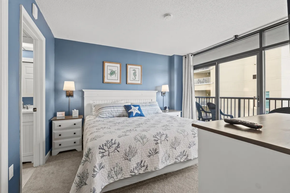 A serene bedroom featuring a comfortable bed positioned next to a window that lets in natural light, a nightstand with a lamp, and decorative wall art. The room exudes a cozy and restful atmosphere ideal for relaxation and unwinding.