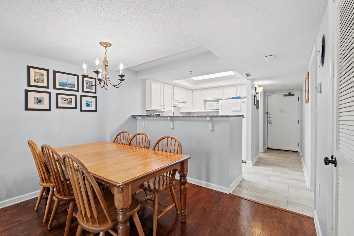 This image focuses on a cozy dining area with a chandelier above, framed pictures on the wall, and a glimpse of the kitchen area beyond. The setup encourages shared meals and social gatherings in a warm, homelike environment.