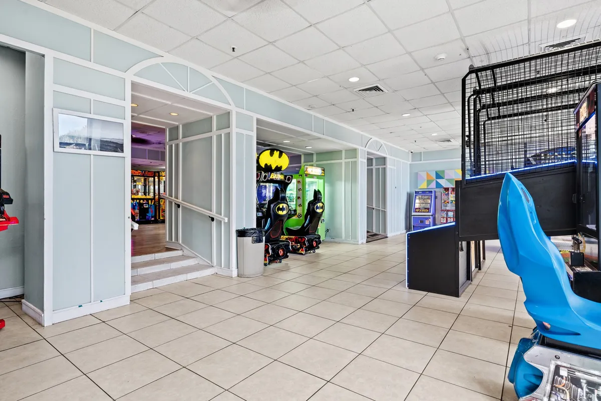 An energetic interior view of the arcade, complete with colorful gaming machines, bright seating, and a staircase leading to additional spaces. The lively atmosphere is ideal for families and guests looking for entertainment beyond the pool.